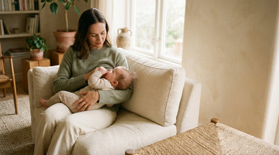A mother reading her baby's early hunger cues on a sofa, the baby turning toward her with a fist at their mouth
