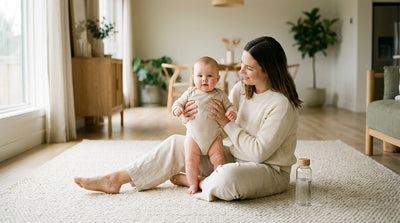 A mother sitting on a rug holding her healthy, alert baby upright on her lap in soft daylight