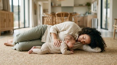 A mother lying on a rug with her baby resting tummy-down on her chest, rubbing the baby's back to settle a windy tummy