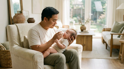 A father giving his baby a bottle in an armchair, watching the baby's cues as they feed