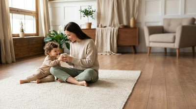 A mother sitting on a rug offering her toddler a small open cup of milk during weaning
