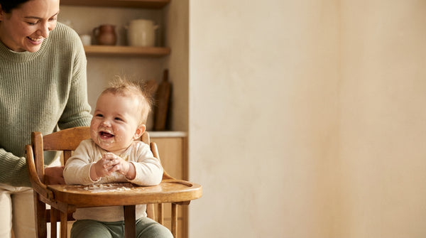 Smiling 7 month old baby in a high chair with food on the tray