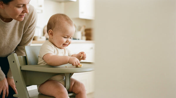 10 month old baby reaching for food in a high chair as a parent leans in