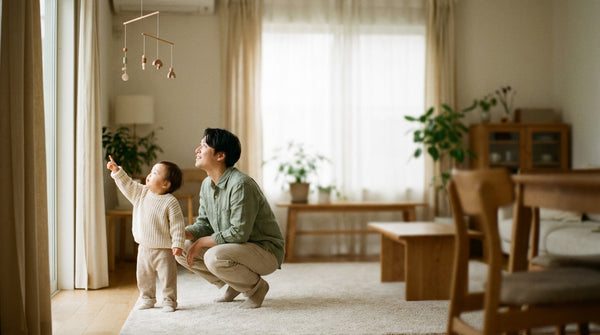 Parent crouching beside their 13 month old reaching up to a hanging mobile