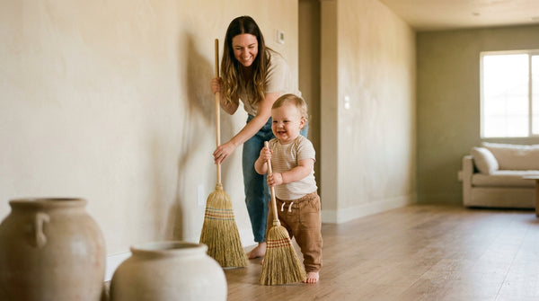 17 month old toddler holding a broom beside a parent sweeping