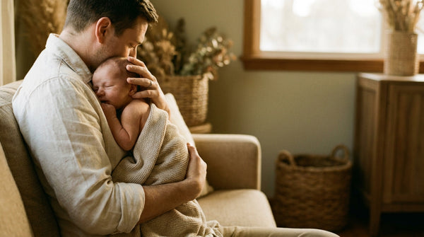 Father cradling his 2 week old baby against his chest in a sunlit armchair