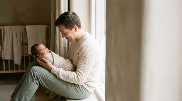 Father sitting on the floor holding his swaddled 4 week old baby on his lap