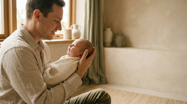 Father sitting on the floor holding his 6 week old baby up in window light