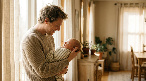 Father standing by a window holding his swaddled 9 week old baby
