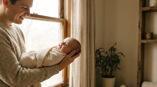 Father holding his 11 week old baby along his forearm by a window