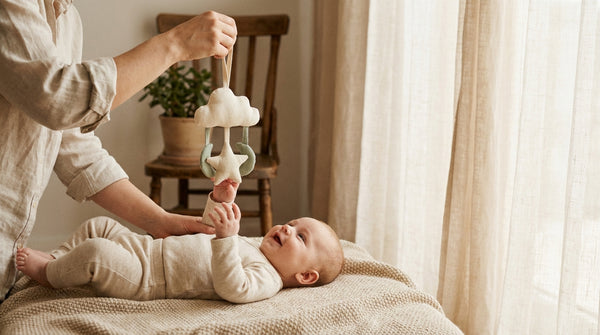 13 week old baby lying down reaching for a cloth mobile held by a parent