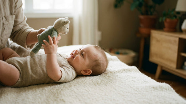 14 week old baby lying on a blanket holding a soft toy above them