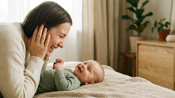 Mother lying beside her smiling 19 week old baby on a bed