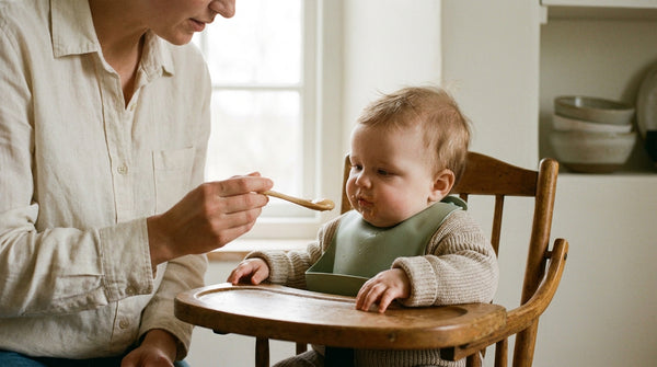 Parent spoon-feeding their 26 week old baby in a wooden high chair